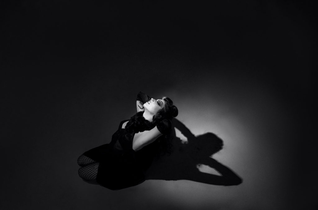 photographie en noir et blanc d'une femme à genoux qui pose sous la lumière d'un spot